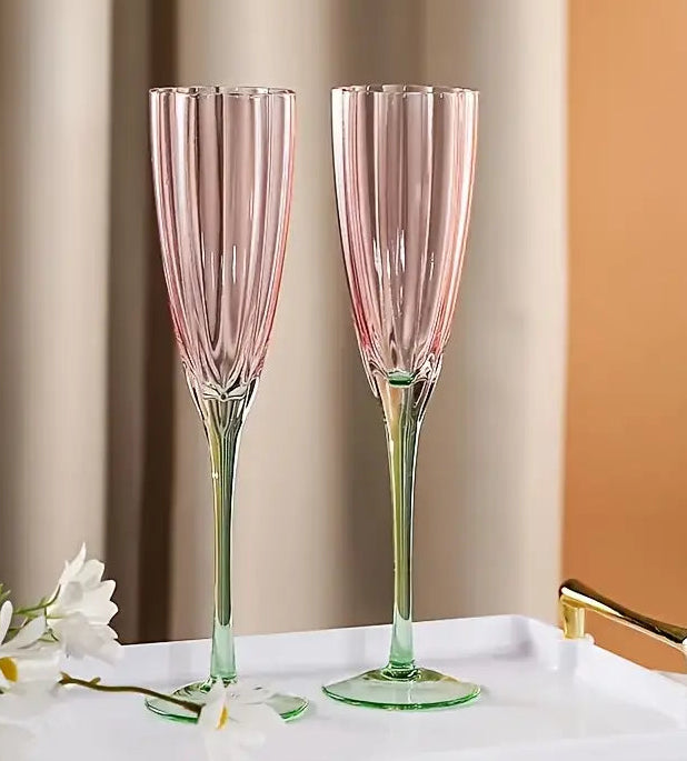 Two pink champagne flutes on a white tray with flowers against a beige wall.