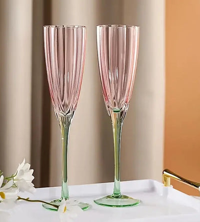 Two pink champagne flutes on a white tray with flowers against a beige wall.